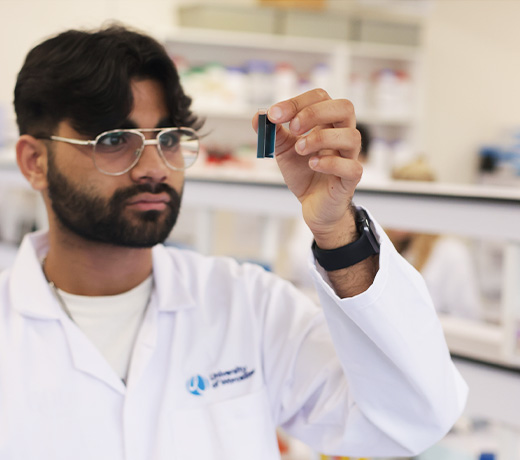 A student in a lab looking at a small sample in a vial