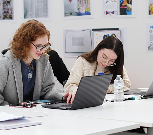 Two design students working on laptops