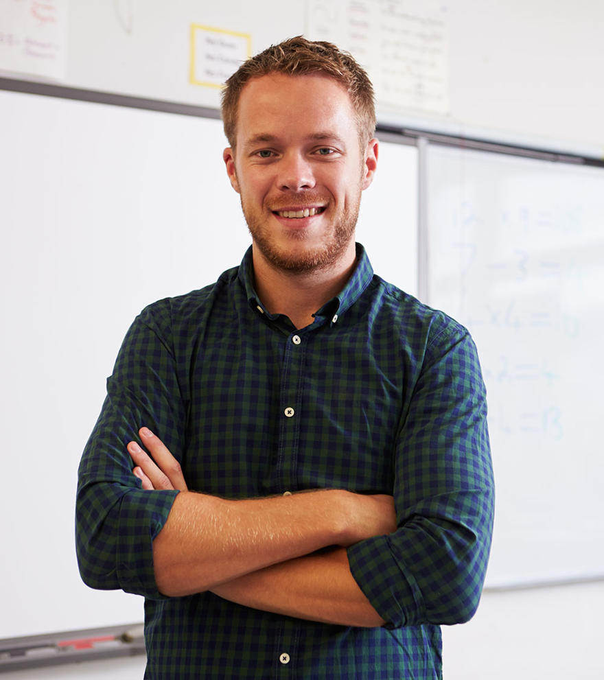 A male teacher is smiling and standing in front of a whiteboard