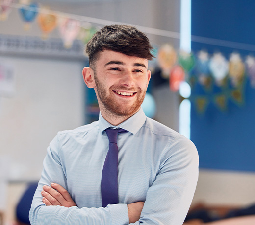 A student stood in a classroom with his arms crossed and smiling