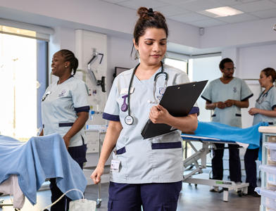 A student nurse looking at a clipboard in a mock hospital ward