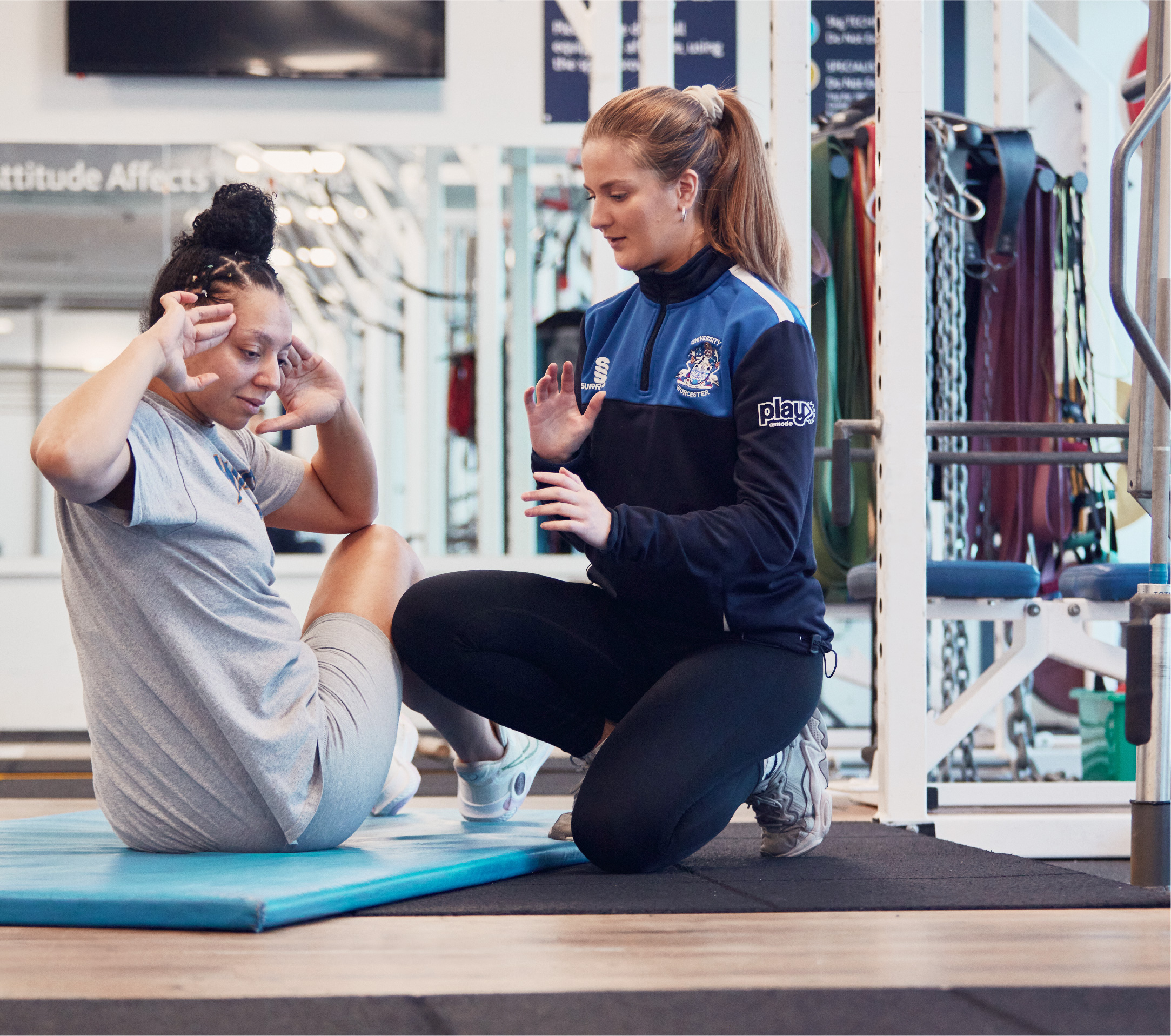 A Sports student kneeling beside a person on an exercise mat in the Riverside gym
