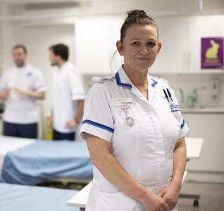 a student nurse is standing in front of a bed smiling at the camera