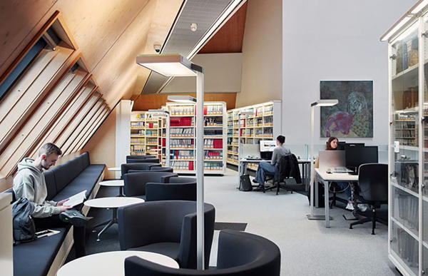 A corner in the the inside of the Hive Library. A student is working near the windows.