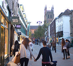People walking away from the camera on Worcester High Street, with the Cathedral in the distance.