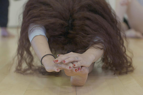 Student with long hair stretching to reach toes on floor