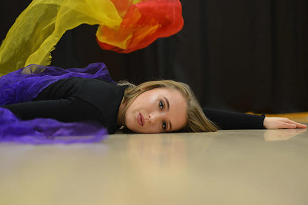 Female student lying on the floor, facing camera with multi-coloured scarves
