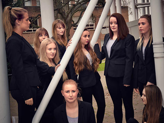 Women in dark suits stand among pillars