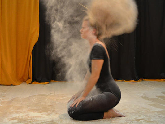 Female student in black throws hair back in cloud of dust