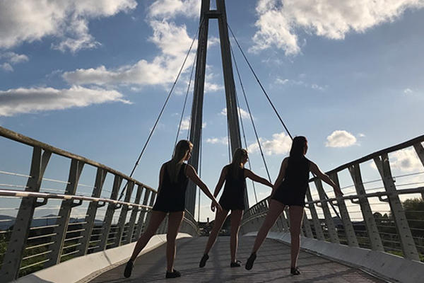 Three dancers on footbridge silhouetted against blue sky