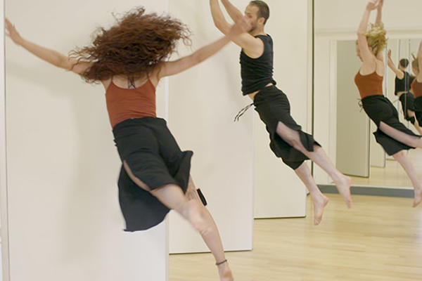 Male and female dancer leap in front of mirror