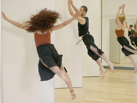 Male and female dancer leap in front of mirror