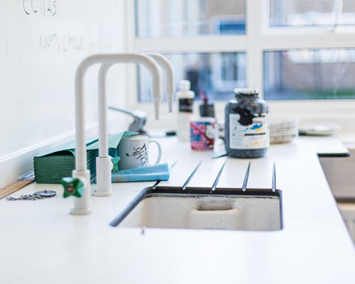 White taps and sink with art materials in the background