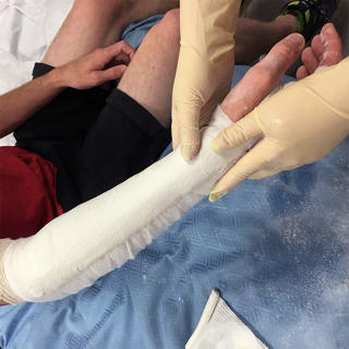 A physician associate student wraps another student's arm in a bandage as part of the physician associate course.