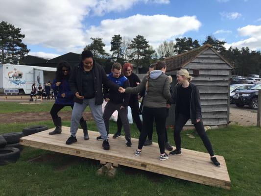 A group of student occupational therapists balancing on a wooden seesaw for a team building activity on our occupational therapy degree.