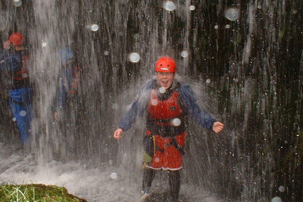 Person in protective clothing and helmet standing under a waterfall