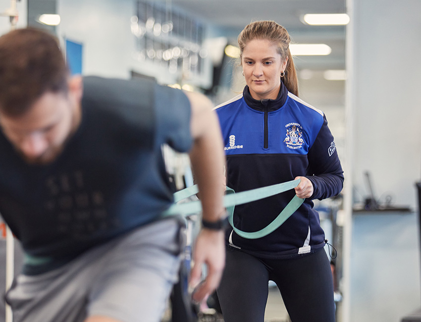 A student coaching a client in the gym using a resistance band
