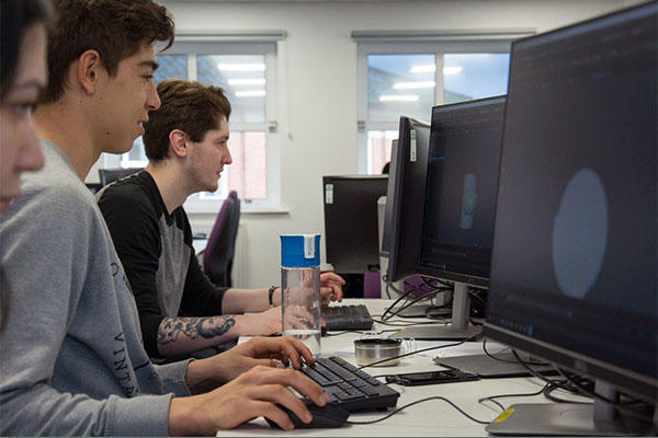 3 students sat at desk using desktop computers