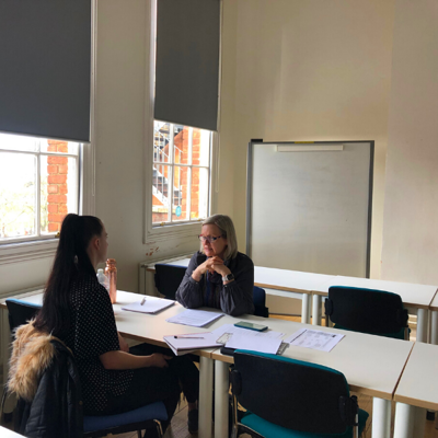 A lecturer and a student sat at a table facing each other, with notes on table