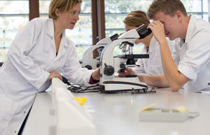 a lecturer is talking to a student that is looking down a microscope