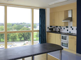 inside a communal kitchen showing a brown table top and a window and a wall cupboard