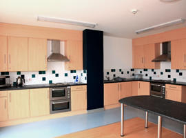 inside a communal kitchen with wall cupboards and fitted ovens