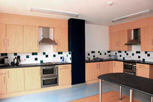 inside a communal kitchen with wall cupboards and fitted ovens