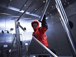 man in a red protective suit inside a laboratory filled with angled metal posts