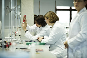 three students in a laboratory setting wearing white protective clothing