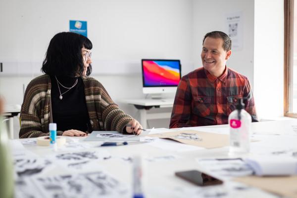 A lecturer sat next to a student with illustrations on table