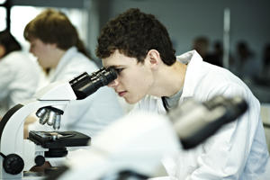 student in a white coat looking into a microscope