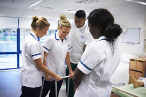 three students in white assisting a student in a frame to walk