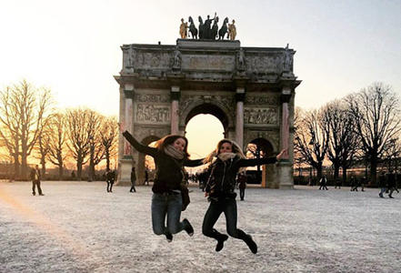 two girls jumping in front of the champs Elysee structure
