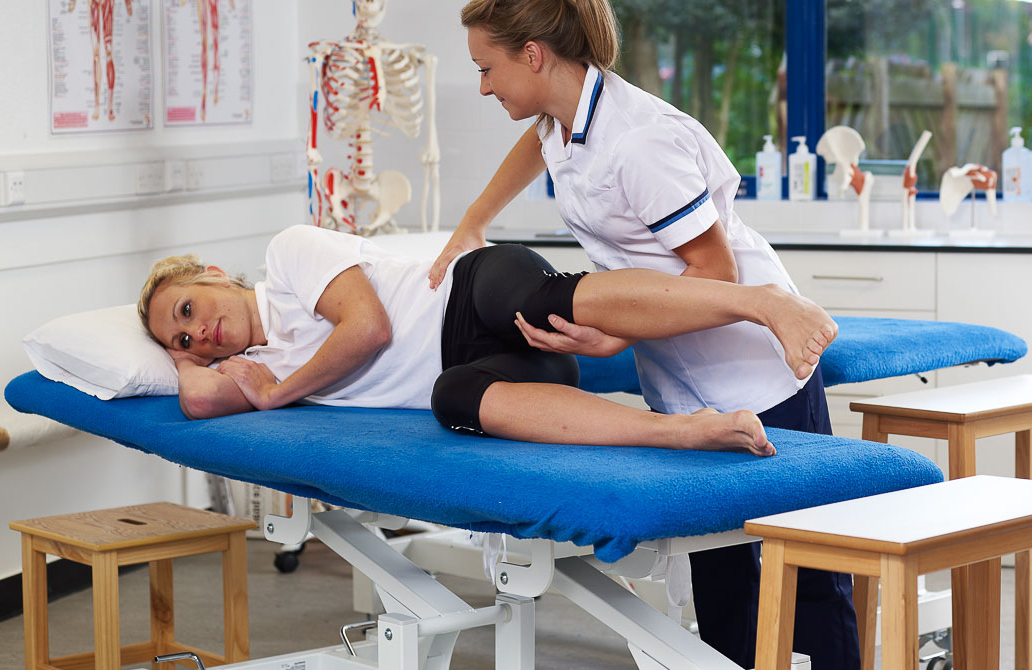 student in a white uniform assisting a student on a bed