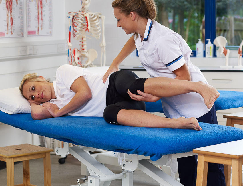 Student in a white uniform assisting a student on a bed