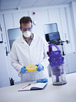 Man in a white coat and mask and blue gloves in front of a work surface