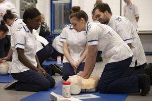 several student nurses kneeling beside a clinical dummy