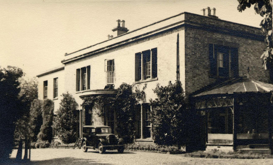 A two-story brick house with shuttered windows and a classic car parked outside