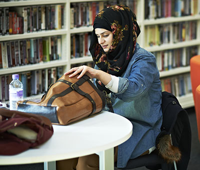 A student, who is wearing a hijab, is sitting in the Hive Library doing some studying.