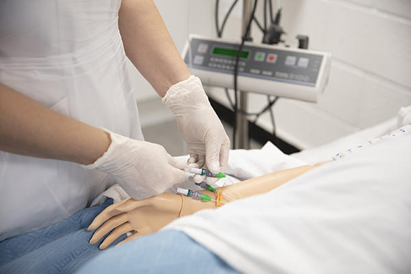 Shot of a dummy being given injected medication by a nurse wearing white rubber gloves.