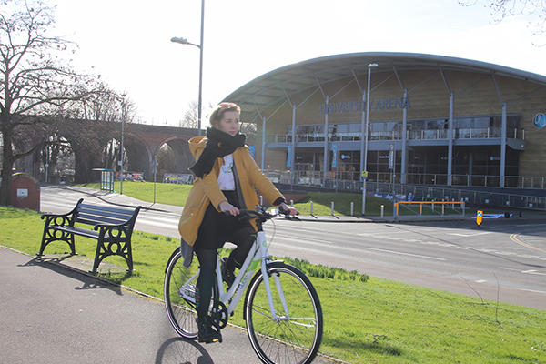 A woman is cycling on a Woo bike outside of the University of Worcester Arena on a winter day