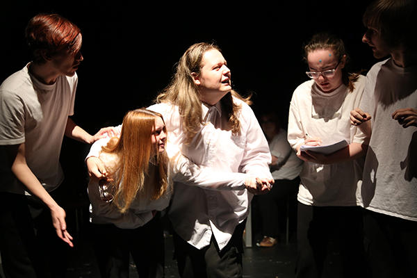 5 students in white shirts acting out a scene of a woman being taken to hospital in labour.