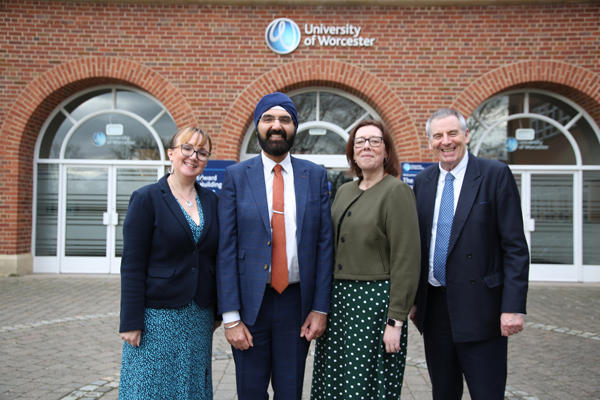 Four people standing outside a building entrance with a University of Worcester logo on building behind
