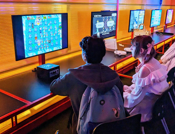 Two people sit looking at a computer screen which is displaying an animated game.