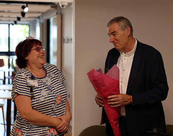 Two people standing looking at each other laughing. One holds a bunch of flowers.