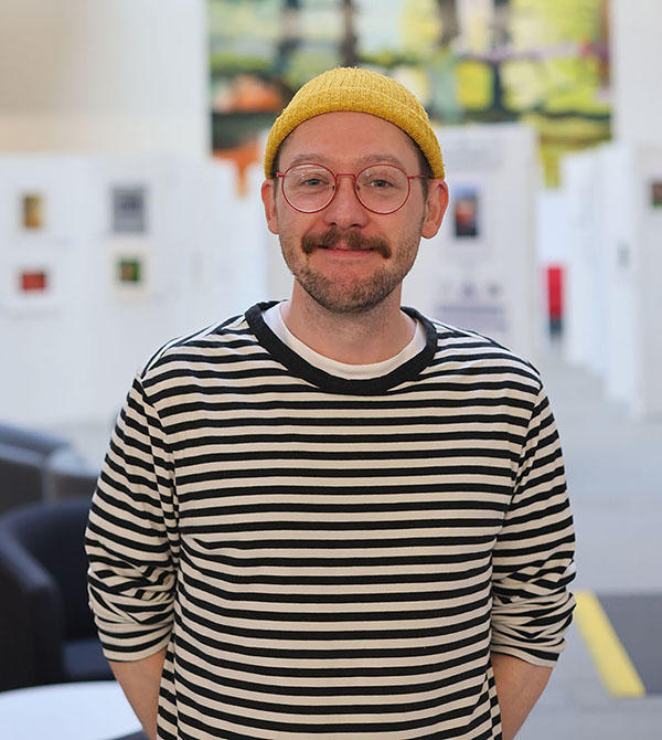 Tom Mandall wearing a black and white stripy top and yellow beanie hat looking at the camera