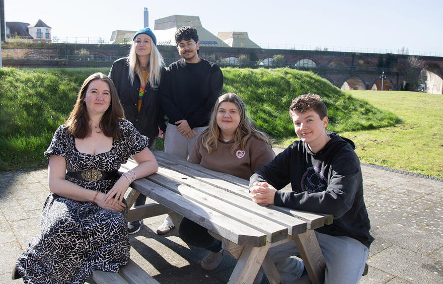 Group of five people sitting at or standing around a picnic bench