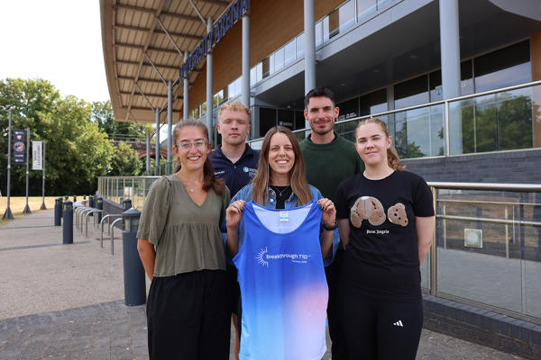 Five people gathered outside a building facing the camera - one holding a running vest