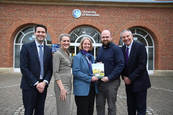 Five people standing posed outside a building - two holding a book