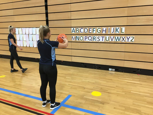 Two Adapted Sports students are throwing netballs against a wall with letter taped to it